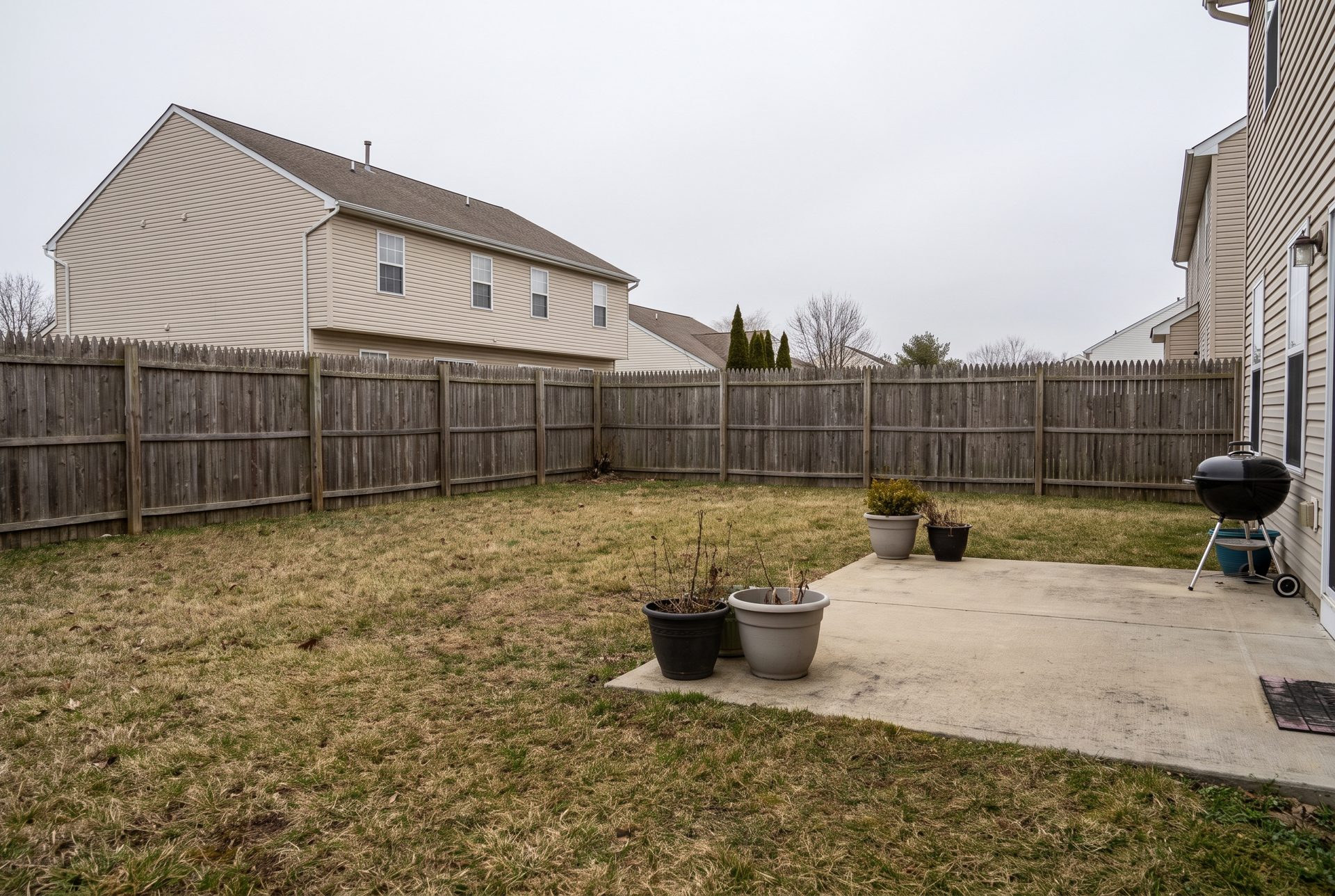 A bare backyard with a wooden fence and the neighbor's house behind it